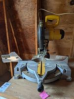 Front view of the DeWalt miter saw showing the saw blade, base, and yellow handle with accumulated sawdust and dust.
