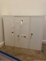 Closed front view of white doll armoire showing four compartment doors with metallic knobs.