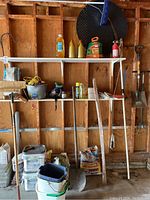 Wide shot showing shelving and wall-mounted garden tools including shovels, hoe, buckets, bags of soil/sand, and various containers.