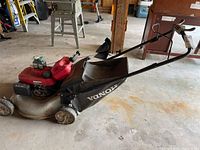Side view of mower with grass bag, engine cover, gas can and oil bottles on deck