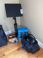 Full lot photo showing the microphone box, Logitech speaker box, Sony video camera with carrying case, and a tripod stand in corner of room.