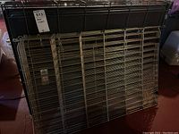 Multiple metal lattice panels and black plastic base trays for two dog crates disassembled and leaning against a surface.