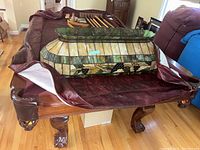 Full view of pool table with maroon cover partially pulled back, showing the pool cues, balls, and stained glass style light fixture resting on the table surface.
