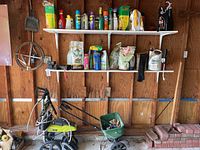 Shelf with assorted plant foods and weed control bottles and bags above Ryobi pressure washer and plastic seed spreader on garage floor