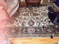 Full view of the rug under furniture showing detailed floral and vine patterns in cream, burgundy, teal, and brown colors.