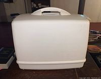 Singer sewing machine stored inside its white plastic carrying case, showing closed case with handle on top