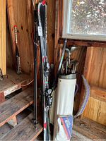 Rossignol skis and ski poles standing upright beside a white TaylorMade golf bag with Howson golf clubs visible inside; children's bow and arrow kit in corner.