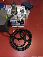 Sump pump system including pump, black corrugated hose, and control panel on red surface next to original box with system branding.