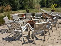 Eight teak chairs arranged in a circle on stone patio around firepit