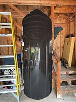 Frontal image showing tall glossy black aerodynamic car roof storage box stored upright in garage environment.