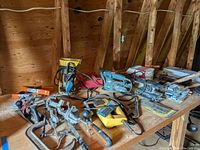 Top view of tools on wooden workbench in an attic space showing power tools, clamps, hand tools, drill bits and screws