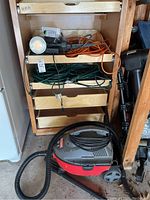 Craftsman vacuum cleaner on floor near wooden shelving with coiled extension cords, spotlight above cords