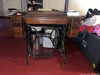 Front view of Singer treadle sewing machine showing oak wood cabinet with drawers and cast iron base with "SINGER" lettering.