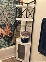 Tall white and black corner shelf placed in bathroom corner next to forest-themed shower curtain with deer design.