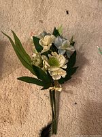 Small bouquet of faux wedding flowers on carpet with cream, blue flowers and green leaves