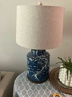 Front view of blue ceramic lamp base with detailed white floral and bird pattern and beige/grey fabric shade.