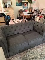 Front view of charcoal grey tufted loveseat showing two cushions and damage on the fabric likely from cats.