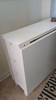 Folded view of white Ikea flip-up table against wall, showing closed flat surface with side drawers visible.
