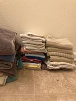Stack of various towels on tile floor including bath towels, hand towels, and washcloths in multiple colors and sizes