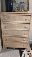 Front view of cream colored wicker dresser with five drawers and matching knobs showing overall condition.
