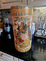 Full view of the tall porcelain vase with colorful floral and bird artwork on a kitchen counter.