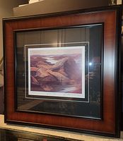 Photos show a professionally framed fine art print by Franklin Carmichael titled Grace Lake. The frame is medium to large size, 22 x 22 inches, with multiple mats and a rich brown wooden frame. The artwork depicts a stylized landscape of rocky hills and a lake in shades of purple and brown.