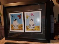 Framed fine art print featuring two prints 'Kitten in Teacup 1' and 'Kitten in Teacup 2' by Maud Lewis in a black wooden frame with double mat.