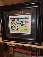Framed Maud Lewis art print showing colorful image of a kingfisher flying with flowering trees and rural houses in background.