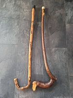 Pair of natural hardwood walking sticks laid flat on dark tile floor showing full length and shape.