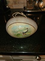 Front view of egg-shaped purse showing one side with bird illustration on cracked textured surface