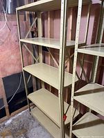 Two beige metal shelving units positioned next to each other in a basement or storage area. Each has five shelves with cross braces visible on the sides and back. Shelves show minor wear and surface scratches.