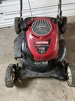 Top view of the mower showing red engine cover with Craftsman and Briggs and Stratton branding, grass residue on black deck and four wheels.