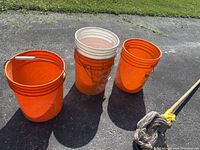 Four orange and white 5-gallon buckets arranged on asphalt outdoors