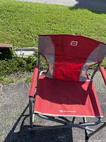 Front view of the Coleman red directors camp chair on pavement and grass background showing fabric and logo details