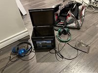 Photo showing black wooden keepsake drawer, two pairs of wired headphones, a Coach wristlet pouch, and a silver Puma gym bag on floor.