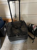Front view of the large black foldable cooler with telescoping handle retracted, visible wear from use, placed next to the small Coors Light backpack cooler on the floor.