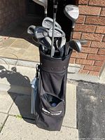 Photo of black Callaway golf bag filled with right-handed golf clubs, outdoors on pavement with brick wall background