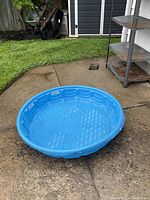 Blue plastic kiddie pool set on concrete surface outside, showing round shape and textured interior.
