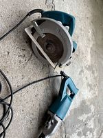 Photo showing Makita skill saw and reciprocating saw lying on concrete floor, cords attached, signs of wear and use visible.