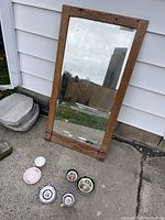Antique mirror with wooden frame leaning against exterior wall showing full view of frame and reflective surface.