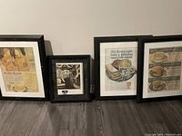 Four framed vintage styled wall art prints leaning against a wall on a wooden floor