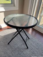 Side view of the round table showing black metal legs and textured glass surface in natural light.