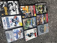 Photo showing full view of 9 PlayStation 2 game cases arranged on pavement: The Getaway, Midnight Club, Tom Clancy Rainbow Six 3, Tiger Woods PGA Tour, NHL 2003, Hot Shots Golf, Madden NFL 2001, SOCOM U.S. Navy SEALs, GTA III.
