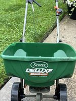 Front view showing green hopper with Scotts Deluxe EdgeGuard branding and black plastic wheels.