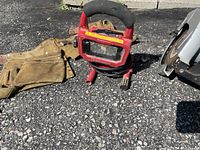 Photo showing a brown leather carpenter's belt, a red portable trouble light with handle and protective cage, and part of the electric skill saw.