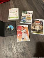 Five video games spread on floor including Wii Fit, Wii Play, EA Sports Active Personal Trainer, Tiger Woods PGA Tour 09 All-Play, plus a black case with GameCube disc.