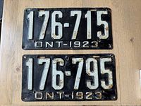 Top view of both black 1923 Ontario license plates showing embossed white numbers 176-715 and 176-795, with wear and rust spots.