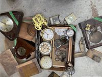 Lot overview showing multiple wooden clock cases, clock faces, and brass clock movements arranged on the floor.
