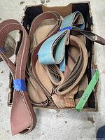 Box containing assorted sanding belts of various sizes and grits, some are blue and some brown.