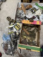 Photo showing assortment of metal and wooden hardware pieces in boxes including brass handles, hinges, screws, decorative plates and chains.